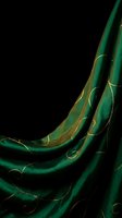 Elegant emerald green silk fabric with golden accents flowing gracefully against black background for luxury fashion and textile design projects.