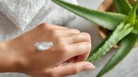 Moisturizing hand cream with aloe vera plant in background on white towel. Natural skincare and beauty concept showing cosmetic product application.
