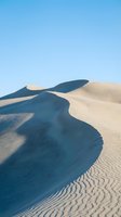 Dramatic sand dunes with flowing curves and deep shadows under clear blue sky creating abstract natural landscape patterns in desert environment.