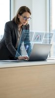 Professional female doctor analyzing medical data on laptop with holographic displays showing anatomical charts and diagnostic information in modern office.