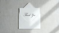 Elegant thank you card with cursive script resting on an open white envelope, placed on a soft linen textured background with natural light.
