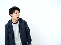 Young Asian man wearing navy blue hoodie and gray shirt, looking surprised with mouth open against white background, isolated for commercial design use.