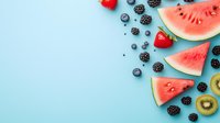 Fresh summer fruits arranged on blue background with watermelon slices, berries, kiwi creating decorative border with copy space for text. Food photography layout.