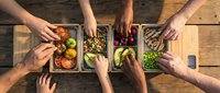 Overhead view of diverse hands sharing fresh vegetables in wooden crates on rustic table, representing community, healthy eating, and sustainable food sharing for culinary and lifestyle content.
