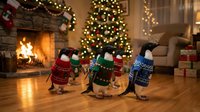 Three adorable penguins in colorful Christmas sweaters waddle across cozy living room with fireplace, decorated tree and warm holiday lights creating festive atmosphere.