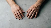 Male hands placed flat on concrete surface showing natural skin texture and masculine features for health and wellness concepts.