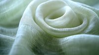 Soft green linen fabric with gentle folds and curves creating an abstract textural pattern with natural light highlighting delicate weave structure.