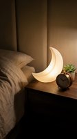 Glowing crescent moon shaped night light on wooden bedside table creates cozy ambient lighting in modern bedroom interior with warm atmosphere.