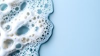 Foamy soap bubbles and suds on light blue background with copy space for cleaning and hygiene concepts in commercial and household applications.