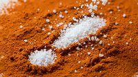 White sea salt crystals scattered on vibrant orange paprika powder creating striking color contrast for culinary and cooking applications.