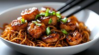 Savory Asian noodles with glazed meatballs, garnished with fresh scallions and sesame seeds, served in white bowl with chopsticks for authentic dining.