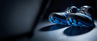Modern athletic running shoes with blue accents on dark surface with dramatic lighting and shadows for sports and fitness concepts.