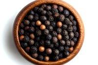 Black peppercorns and allspice berries in wooden bowl on white background, overhead view of aromatic spices for cooking and seasoning food.