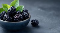 Fresh ripe blackberries in dark ceramic bowl with mint leaves on black stone background, moody food photography with selective focus and copy space.