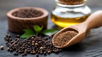 Ground and whole black peppercorns with olive oil on dark stone background, wooden spoon with freshly ground pepper and green leaves for cooking.