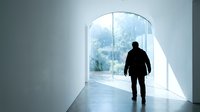 Silhouette of male professional standing in modern corridor facing large curved window with natural light and outdoor view, representing opportunity and future vision.