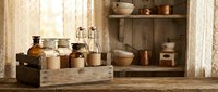 Rustic kitchen pantry with vintage glass jars, ceramic bowls and wooden shelves displaying traditional storage containers in warm natural lighting.