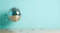 Shiny disco ball hanging against turquoise wall with scattered confetti on wooden floor for party celebration and retro dance events.