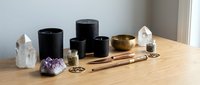 Arranged collection of black candles, crystals, and wooden tools on natural wood surface for meditation and spiritual wellness practices.