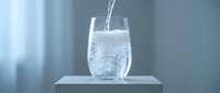 Fresh sparkling water being poured into clear glass on white surface with bubbles and splash creating refreshing beverage moment for healthy lifestyle.