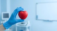 Medical professional in blue gloves holding red heart symbol in modern healthcare facility representing cardiology and heart health care.