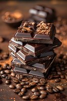 Dark chocolate pieces stacked with coffee beans and cocoa powder on wooden background, rich brown tones create appetizing composition for food photography.