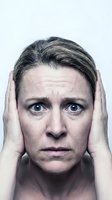 Middle-aged Caucasian woman with gray hair holding head in hands showing stress, anxiety, headache, mental health struggles, emotional distress on white background.