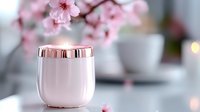 Pink ceramic cup with rose gold metallic rim against soft blurred background with delicate cherry blossoms and white teacups, creating serene spring atmosphere.