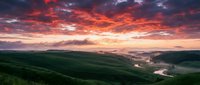 Dramatic sunset over rolling green hills with winding river and valley landscape, vibrant orange and red sky with clouds, scenic nature background for travel and environmental projects.