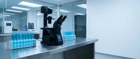 Modern laboratory microscope on steel counter with blue test tubes in sterile medical research facility for scientific analysis and experimentation.
