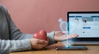 Person holding a red heart and a glowing digital light bulb hologram near a laptop, symbolizing online connection and creative social media ideas.