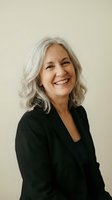 Confident mature businesswoman with gray hair smiling in black blazer against neutral background for professional corporate headshot photography.