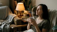 Young Hispanic woman relaxing on cozy sofa with hot beverage in warm living room with soft lamp lighting for evening comfort and wellness lifestyle.