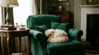 Ginger cat relaxing on emerald green velvet armchair in classic living room with fireplace, wooden side table, lamp and traditional decor for home interior design projects.