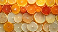 Fresh citrus slices arranged in rows showing variety of oranges, blood oranges, grapefruits and lemons creating colorful gradient pattern on white background.
