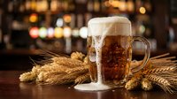 Fresh amber beer with creamy foam in glass mug on wooden bar counter with wheat stalks, warm pub atmosphere with blurred lights background for beverage advertising.