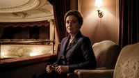 Professional businesswoman in elegant suit sitting in luxury theater box with ornate interior and warm lighting for corporate and entertainment concepts.