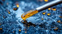 Glass dropper with golden liquid against blue water drops background, macro photography showing amber oil or extract falling in artistic composition.