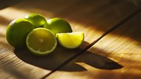 Fresh lime fruits and sliced wedges on wooden cutting board in dramatic natural lighting, creating moody atmosphere for cocktail and culinary photography.