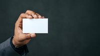 Businessman holding blank white business card in hand against dark background, suitable for corporate branding and professional networking materials.