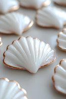 White porcelain seashell-shaped plates with delicate gold trim edges arranged on light surface, creating elegant coastal table setting for fine dining experience.
