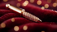 Luxury rose gold fountain pen with diamond pattern on burgundy velvet fabric background with soft bokeh lights creating elegant atmosphere.