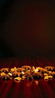 Star anise and dried citrus peel arranged on red wood surface with dark background, suitable for culinary, spice, and food styling projects.