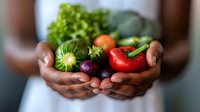 Fresh organic vegetables held in cupped hands including tomatoes, eggplant, zucchini and leafy greens representing healthy eating and farm to table concept.