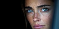 Close up portrait of young woman with intense blue eyes and natural freckles on dark background, dramatic lighting highlights facial features and creates moody atmosphere.