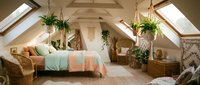 Cozy attic bedroom with skylights, exposed beams, plants and warm natural lighting creating peaceful bohemian interior design atmosphere.