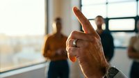 Mature male hand with ring and watch pointing index finger up during business meeting with colleagues in modern office.