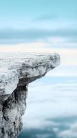 Dramatic rocky cliff edge overlooking misty blue horizon, creating sense of height and adventure against soft pastel sky background. Perfect for themes of risk and challenge.