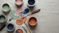 Artist workspace with colorful paint cans, brushes and mixed pigments on neutral surface for creative projects and home renovation tasks.