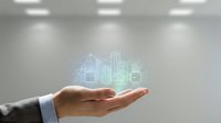 Businessman hand holding glowing holographic cityscape with buildings and digital architecture projection for real estate, urban development, and smart city technology concepts.